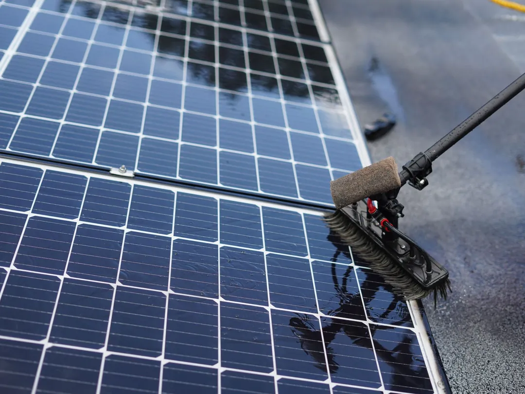 Solar panels being washed with a water-fed brush to clear dirt and grime from the glass