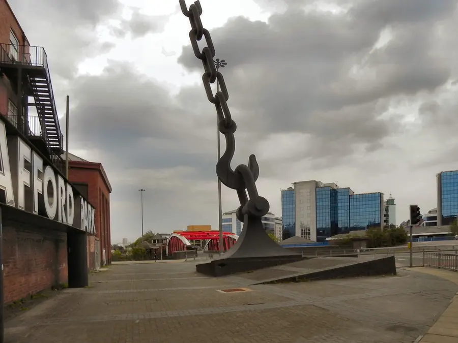The Skyhook sculpture, a giant steel chain and hook, at the Trafford Park entrance with the industrial estate's office blocks behind